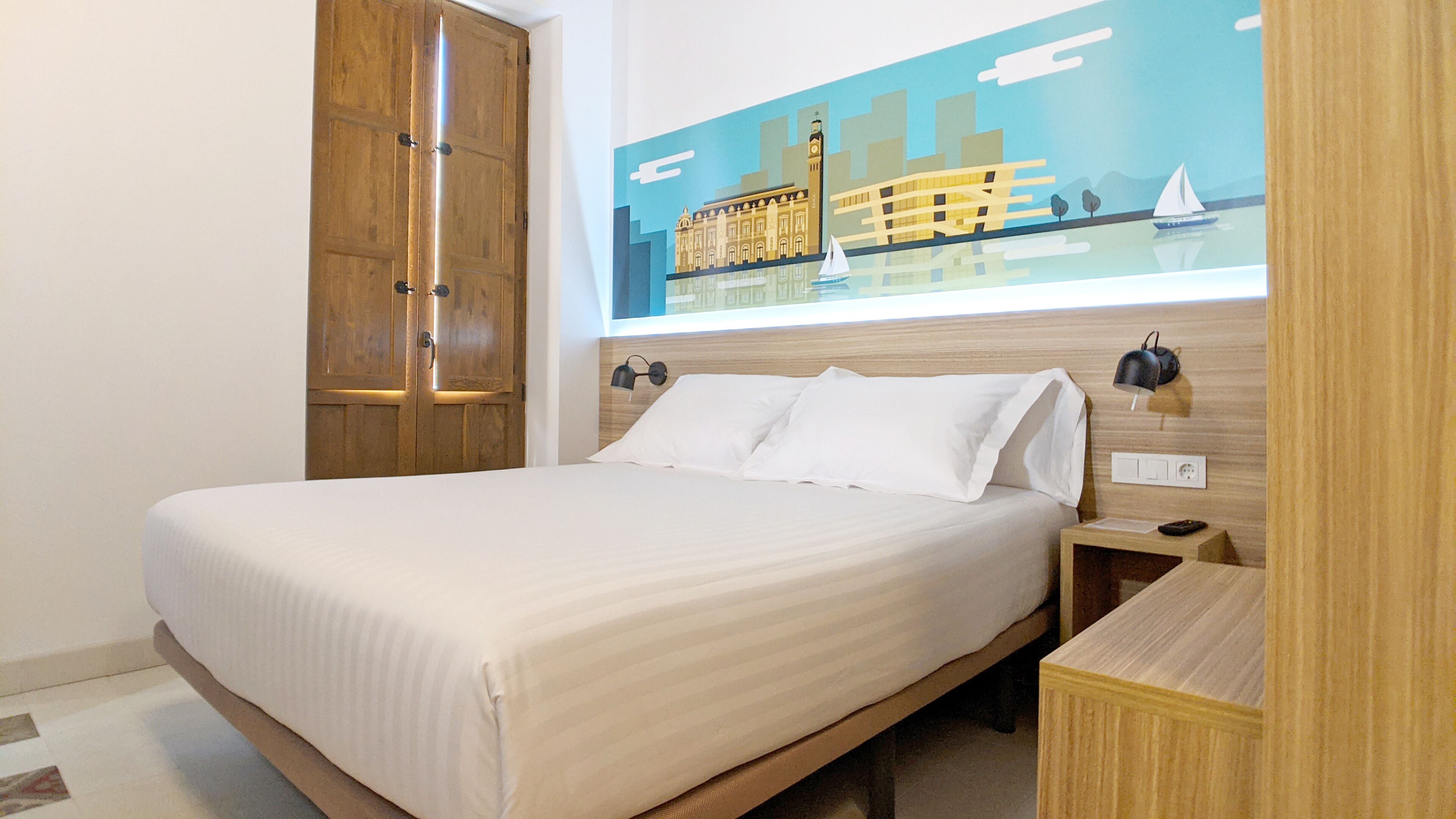 A hotel room with a bed, wooden wardrobe, nightstand, and a wall mural.
