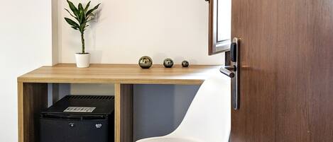 A compact office space with a desk, a white chair, a potted plant, and a black recycling bin.