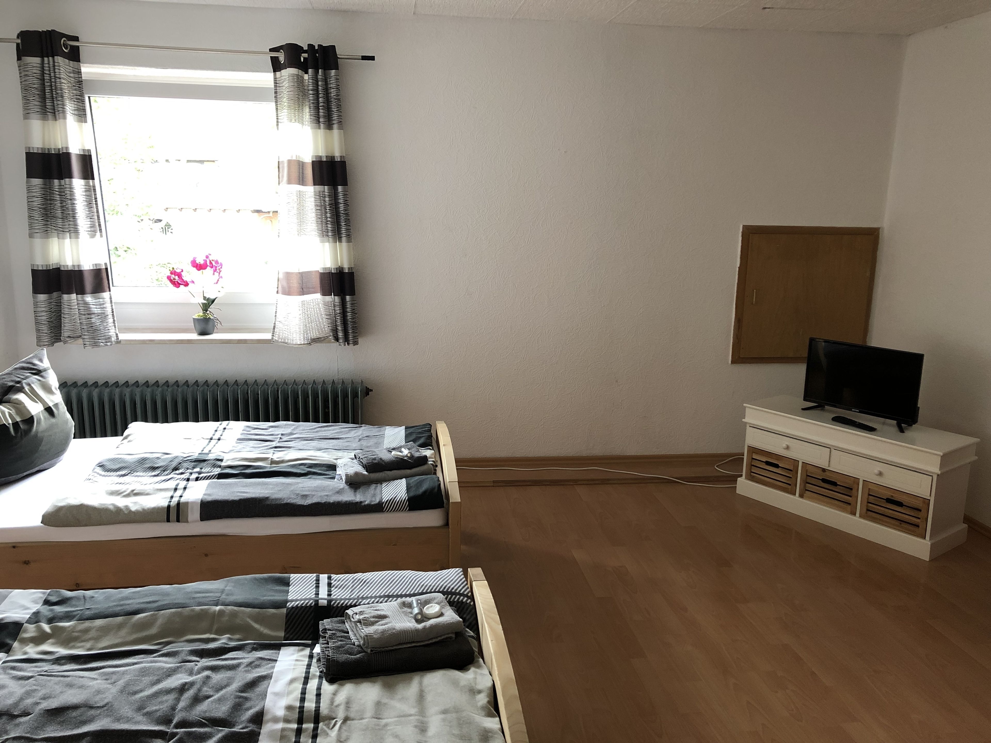 Ein Schlafzimmer mit zwei Betten, einem Fernseher auf einer Kommode und einem Fenster mit Vorhängen.