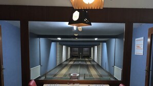 A bowling alley with a long, rectangular table and red chairs. - Hostel Wendt (Fintel)