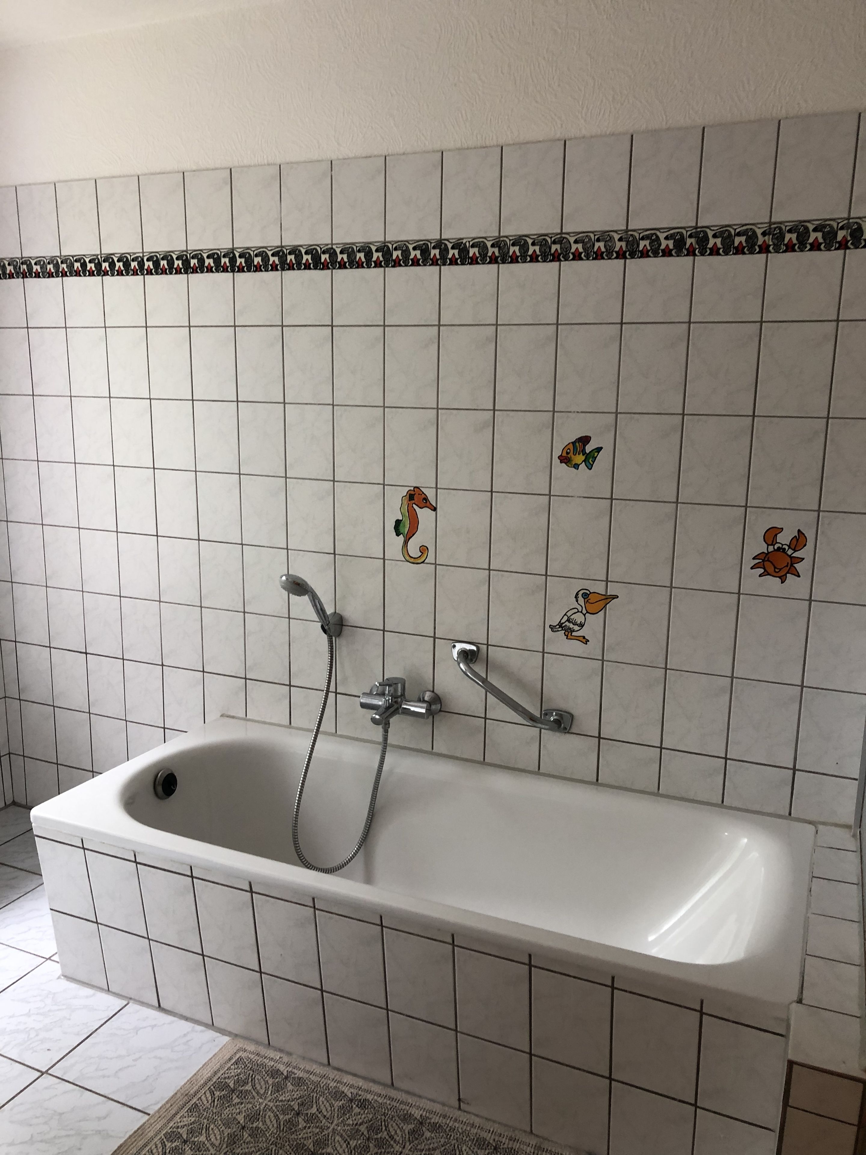 A bathroom with a white bathtub, a shower, and a tiled wall with decorative sea creature stickers.