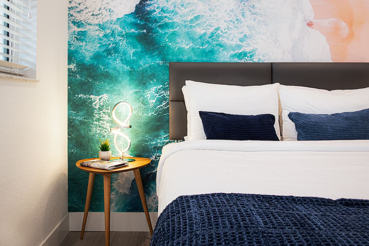 Un dormitorio con cama, una mesita de noche con lámpara y un mural en la pared.