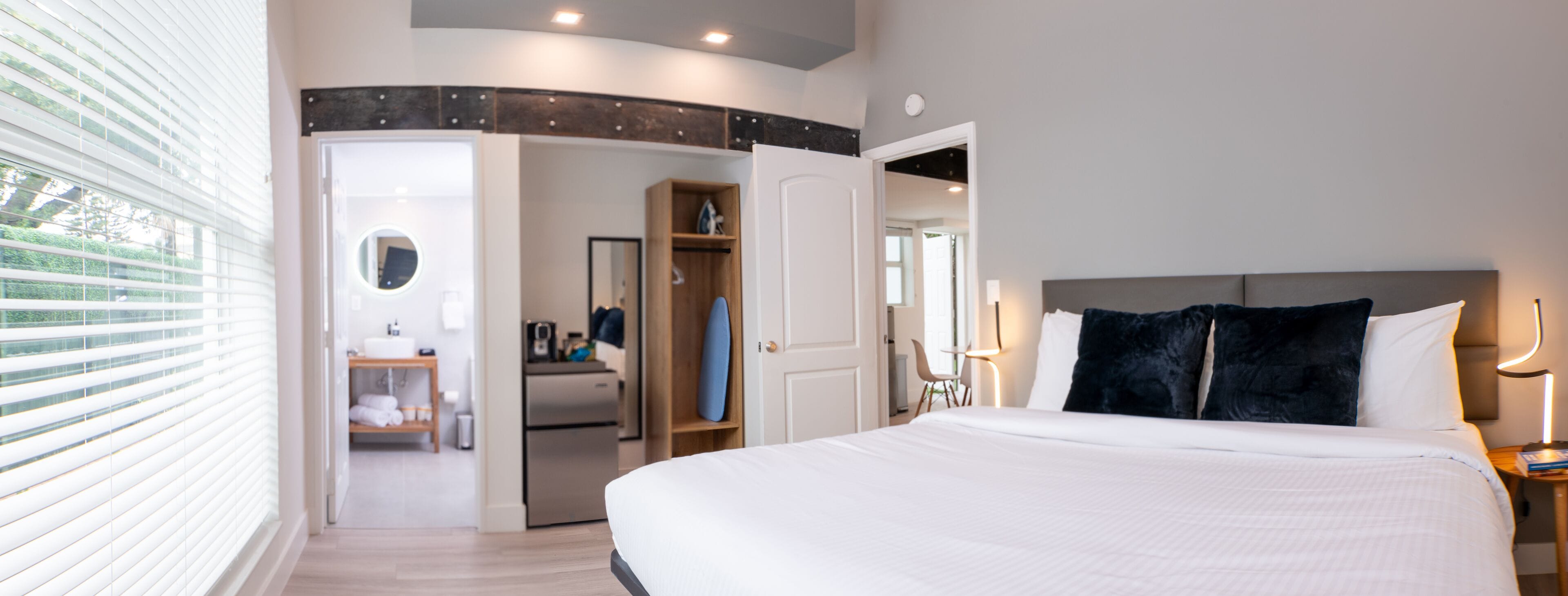 Ein modernes Hotelzimmer mit einem großen Bett, einem begehbaren Kleiderschrank, einem Badezimmer mit Spiegel und Blick aus dem Fenster.
