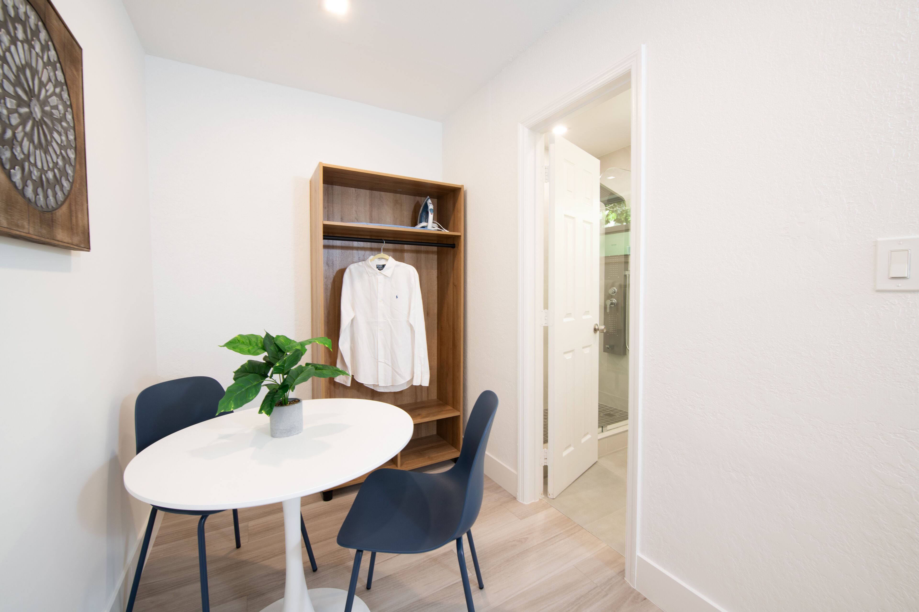 A small room with a white table, two chairs, a wooden wardrobe, and a potted plant.