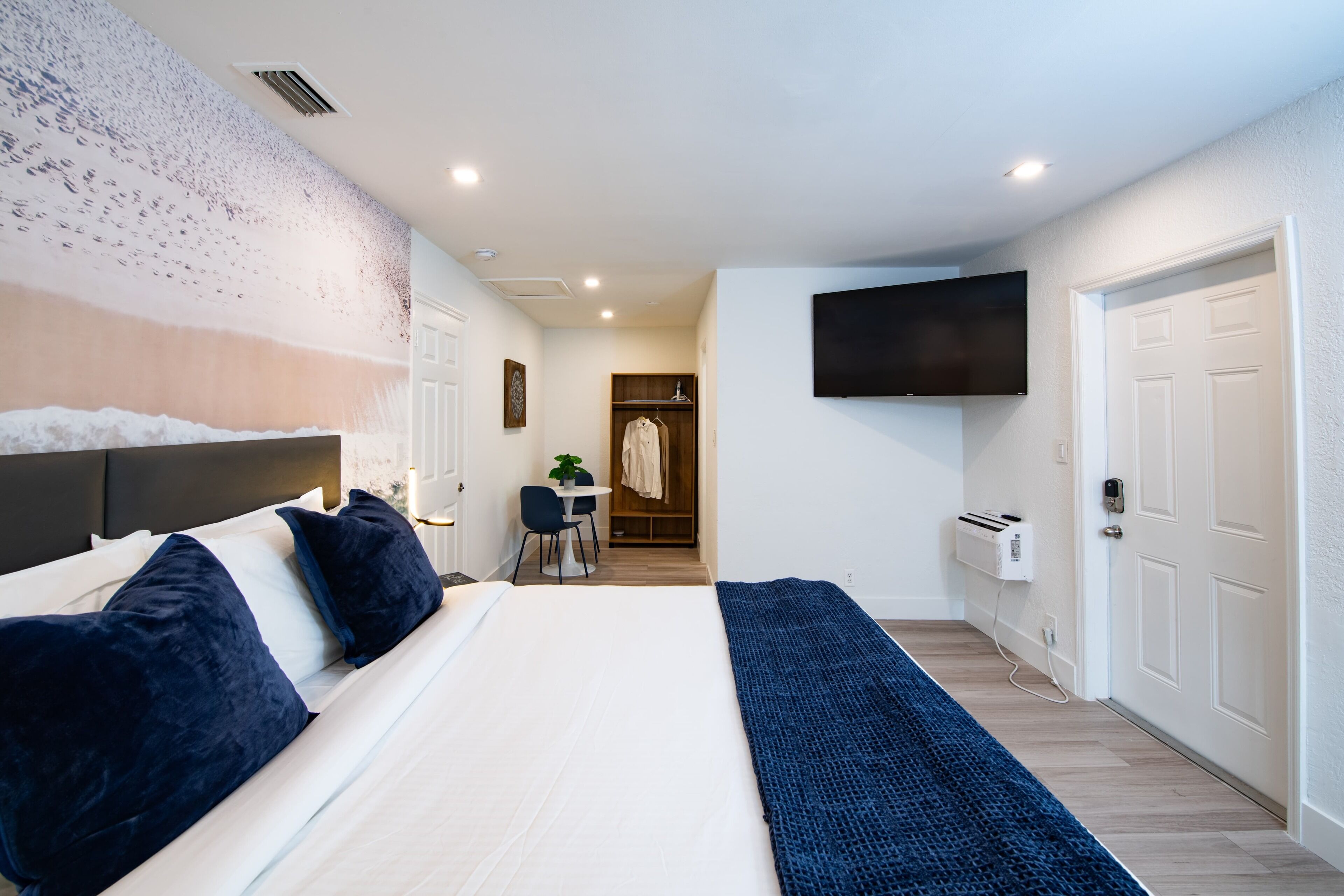 Une chambre d’hôtel avec un grand lit, un bureau avec une chaise, un téléviseur fixé au mur et un porte-manteau.