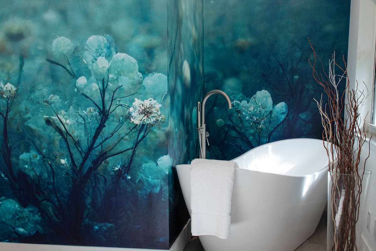 Un baño con un gran mural de una escena forestal, una bañera independiente y un florero de vidrio con ramas.