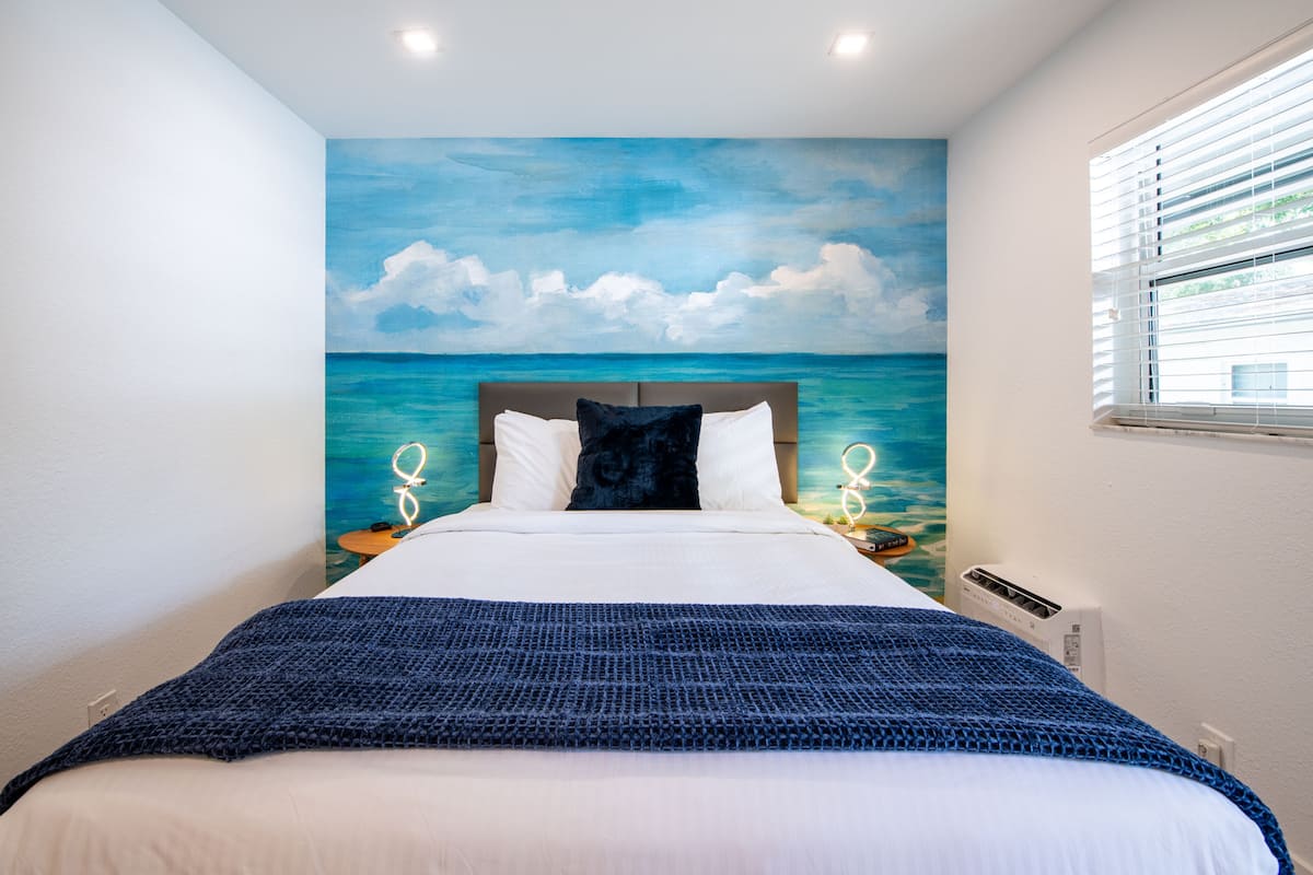 Un dormitorio con cama, vistas al mar a través de una ventana y una lámpara en el techo.