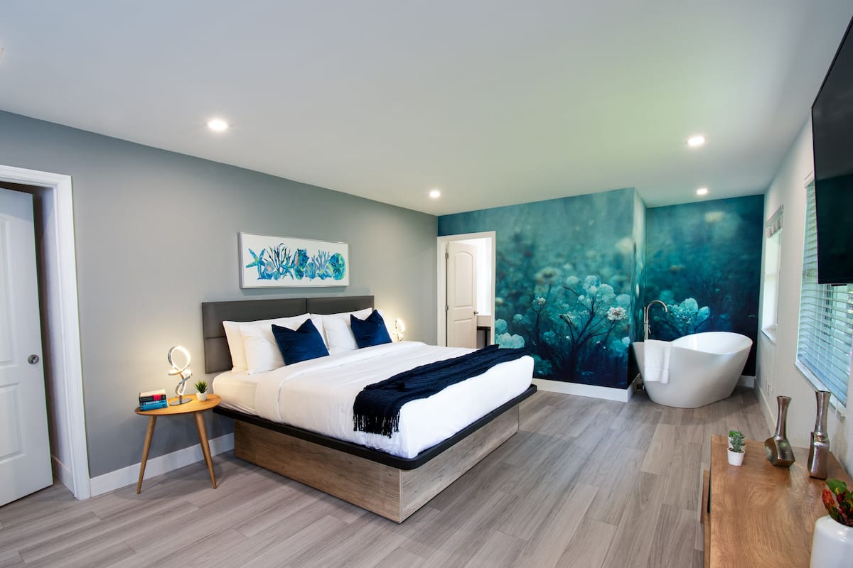 Un dormitorio moderno con una cama grande, un tocador con bañera y un mural en la pared.