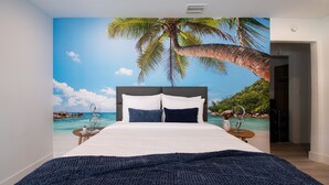 Een slaapkamer met een bed, nachtkastjes en een groot wanddecor van een strandgezicht.