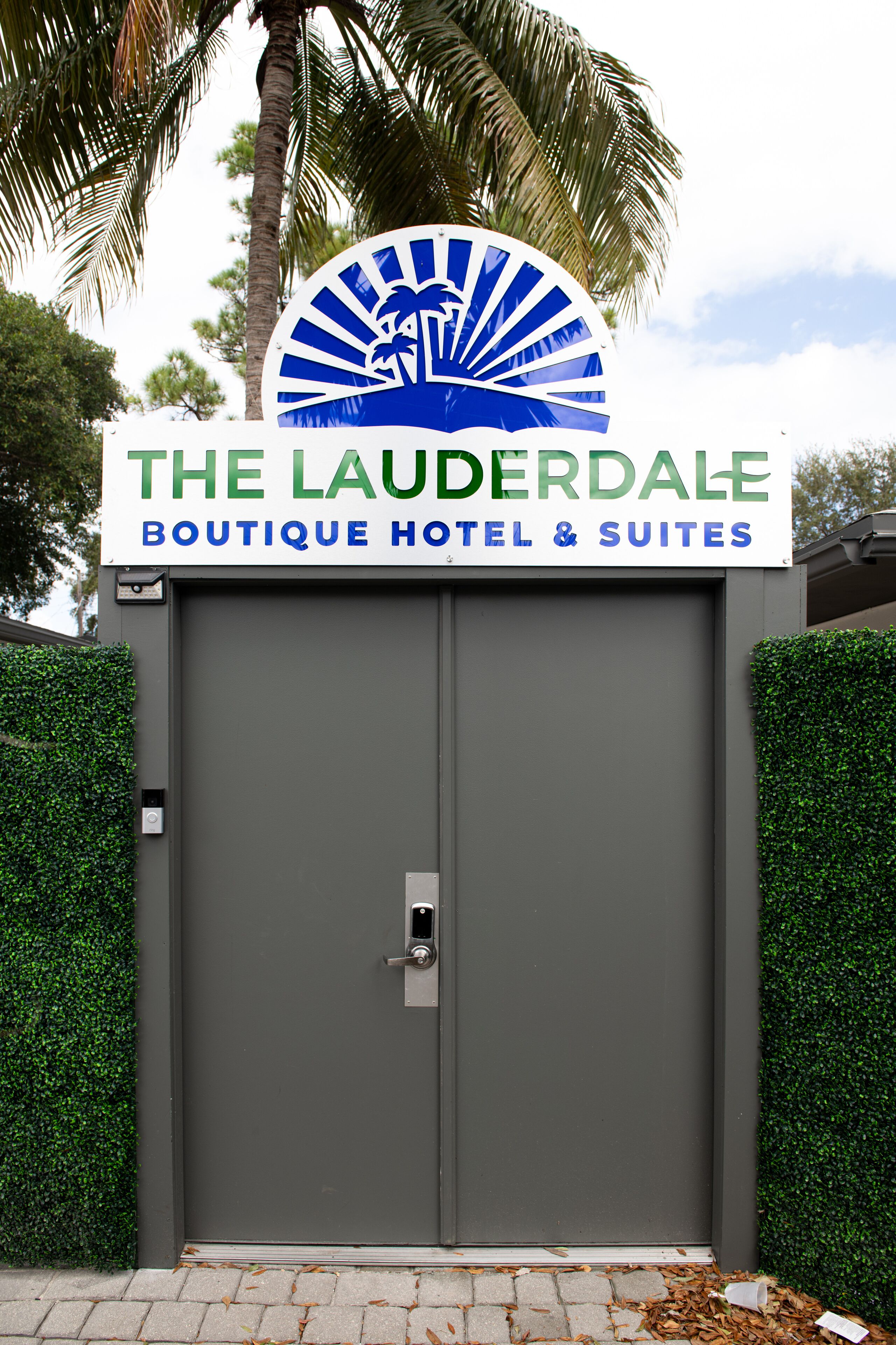 L’entrée d’un hôtel, avec une enseigne indiquant « The Lauderdale Boutique Hotel & Suites » et un palmier en arrière-plan.