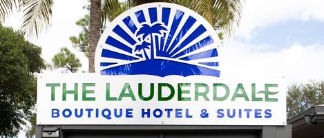L’entrée d’un hôtel, avec une enseigne indiquant « The Lauderdale Boutique Hotel & Suites » et un palmier en arrière-plan.