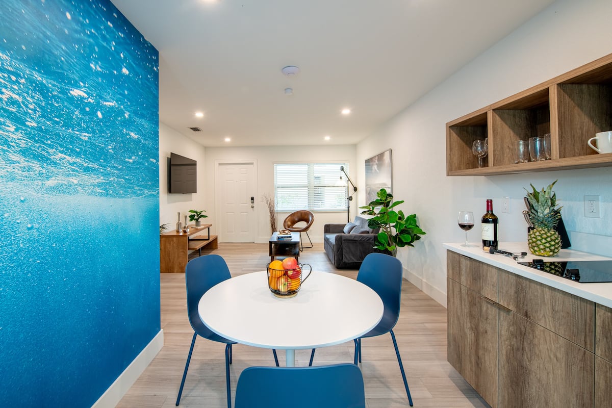 Una cocina moderna con encimera blanca, sillas azules y un frutero.