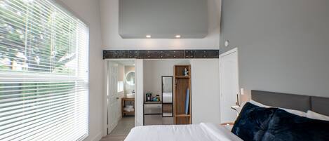 A modern bedroom with a large bed, a walk-in closet, and a bathroom visible through an open door.