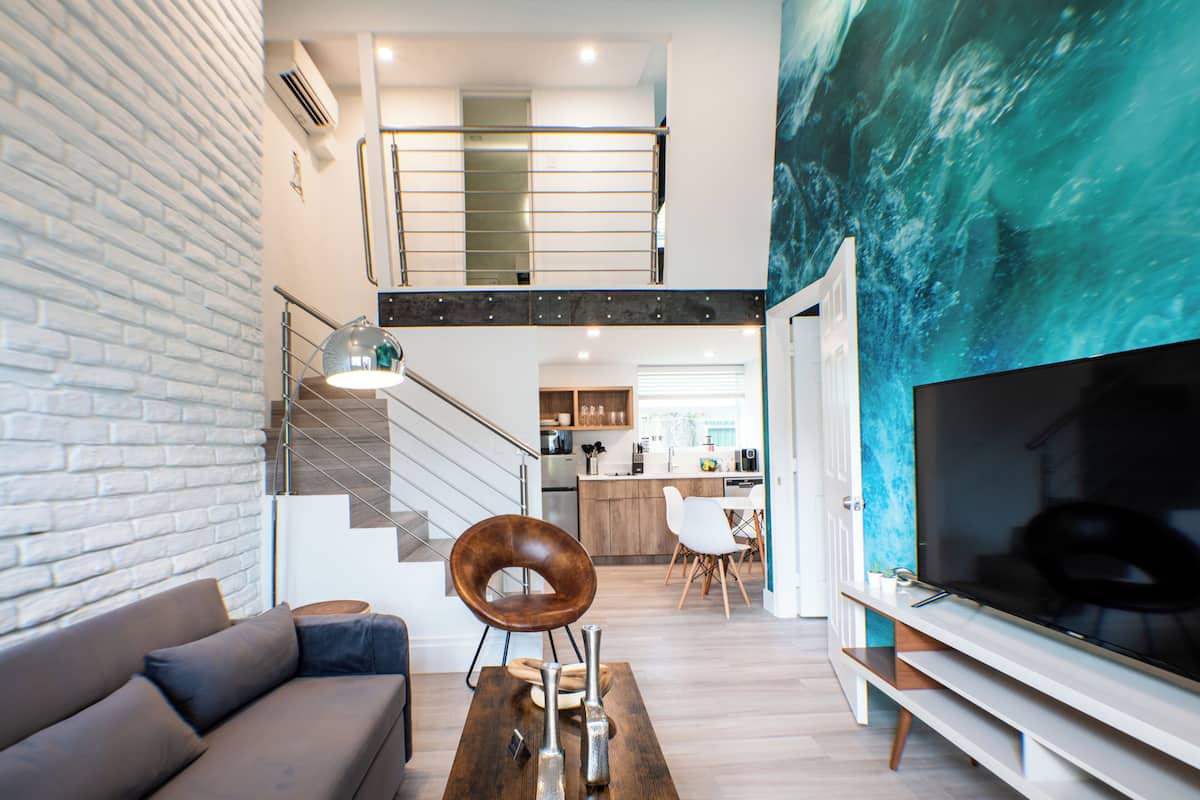 Una sala de estar moderna con un sofá, una mesa de centro y un televisor. Se ve una escalera que sube a un nivel superior.