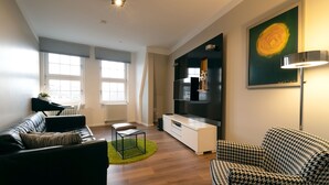 Een moderne woonkamer met een zwarte leren bank, een gestreepte fauteuil, een witte tv-meubel en een groot schilderij aan de muur.