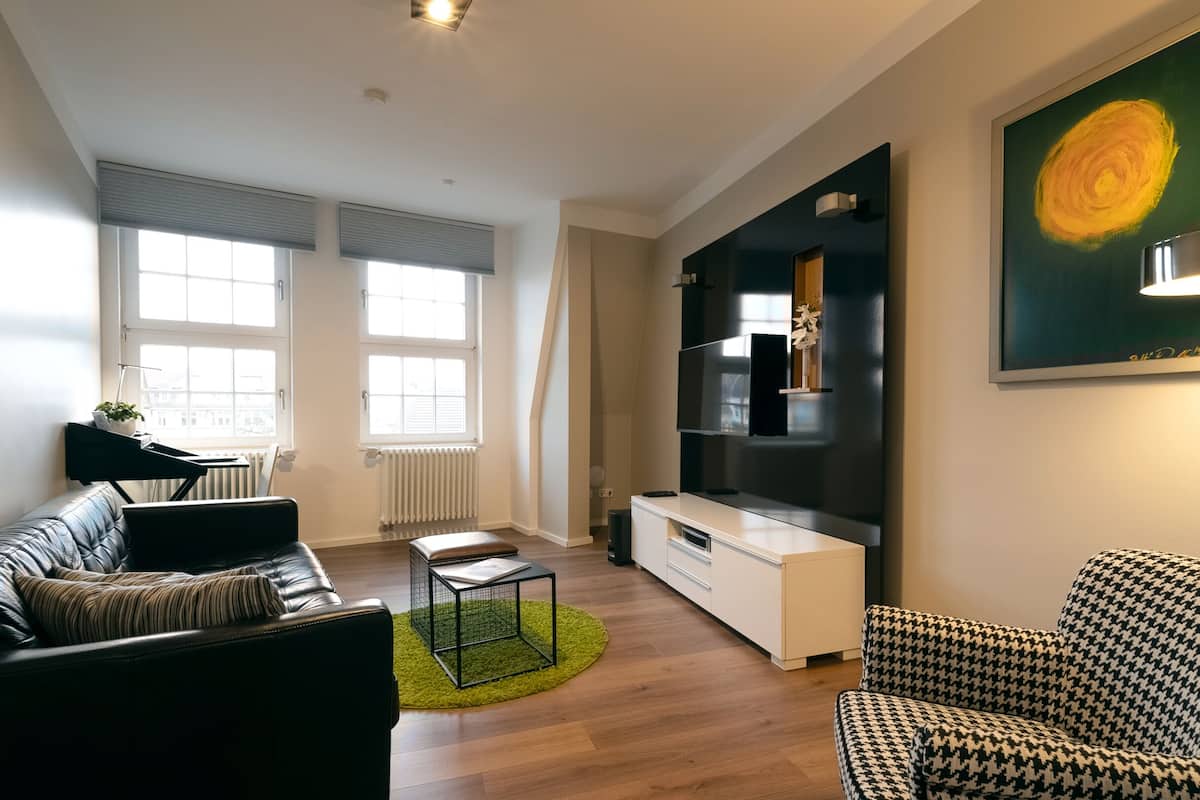 Una sala de estar moderna con un sofá de cuero negro, un sillón estampado, un armario blanco y un cuadro grande en la pared.