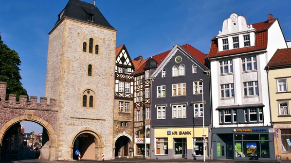 A historic stone tower with a clock, a traditional half-timbered building, and a modern building with a VR Bank sign. - Carl.22 City Appartements (Eisenach)