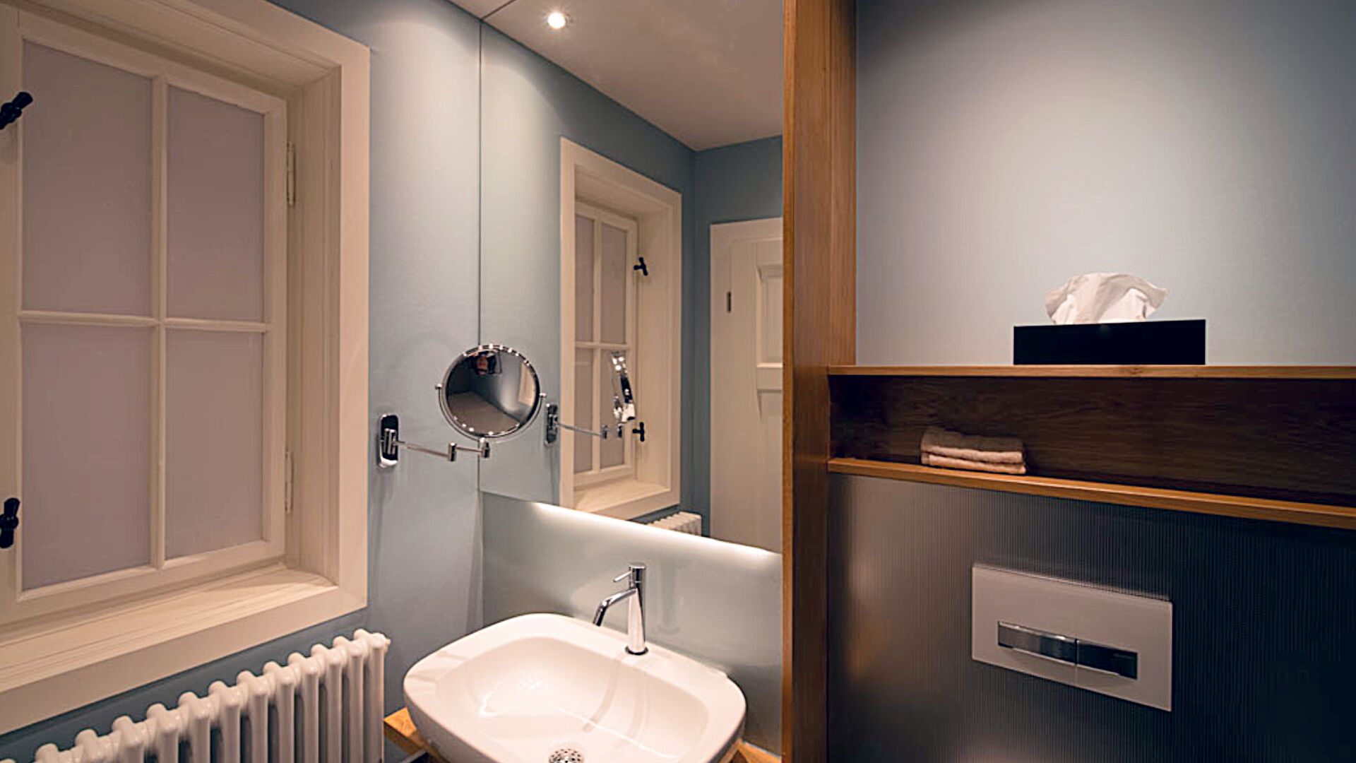 A modern bathroom with a white sink, a mirror, and a towel shelf.