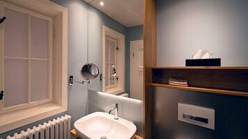 A modern bathroom with a white sink, a mirror, and a towel shelf.