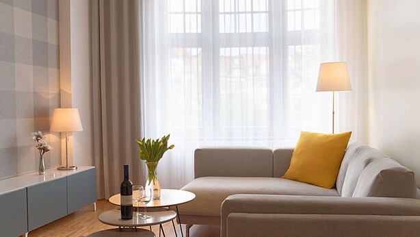 Een moderne woonkamer met een bank, een klein rond tafeltje, een wijnfles en een vaas met bloemen.