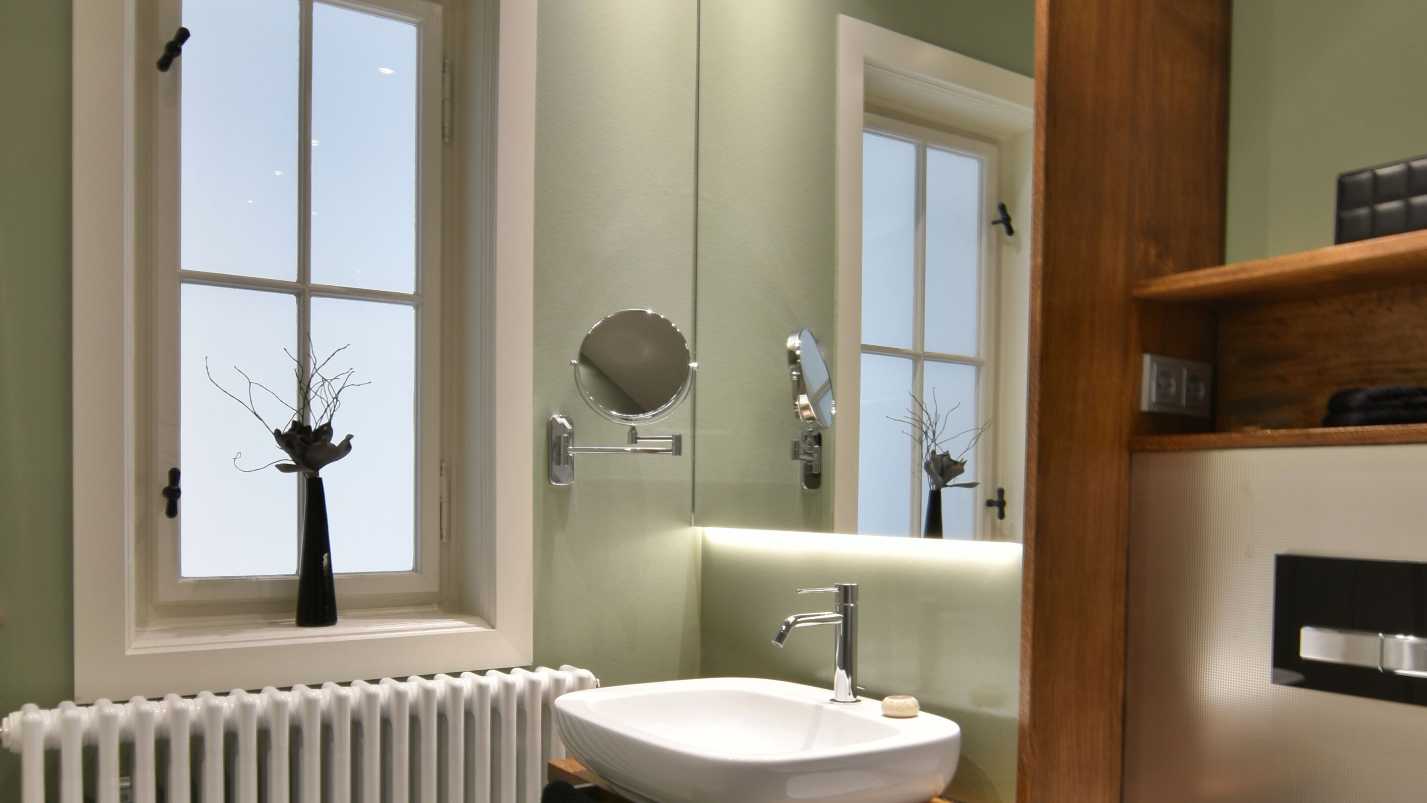 Ein Badezimmer mit Waschbecken, Spiegel und Fenster mit Blick auf kahle Äste.