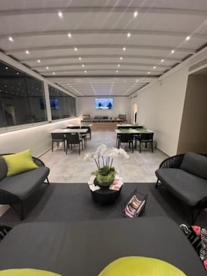 A modern hotel lobby with a central seating area, a flat-screen TV, and a large window providing a view of the cityscape. - Elite Accommodations & Hydromassage Pool (Reggio Calabria)