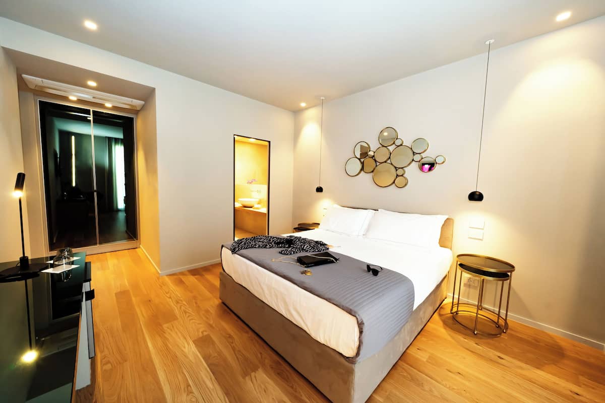 Quarto moderno com uma cama grande, mesas de cabeceira, um espelho e uma obra de arte na parede.