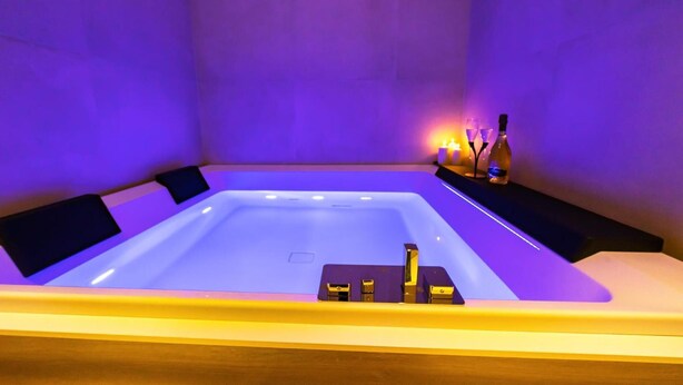 Ein Wellnessraum mit einer großen Badewanne, einer Holzbank und einem Regal mit Kerzen und Flaschen.