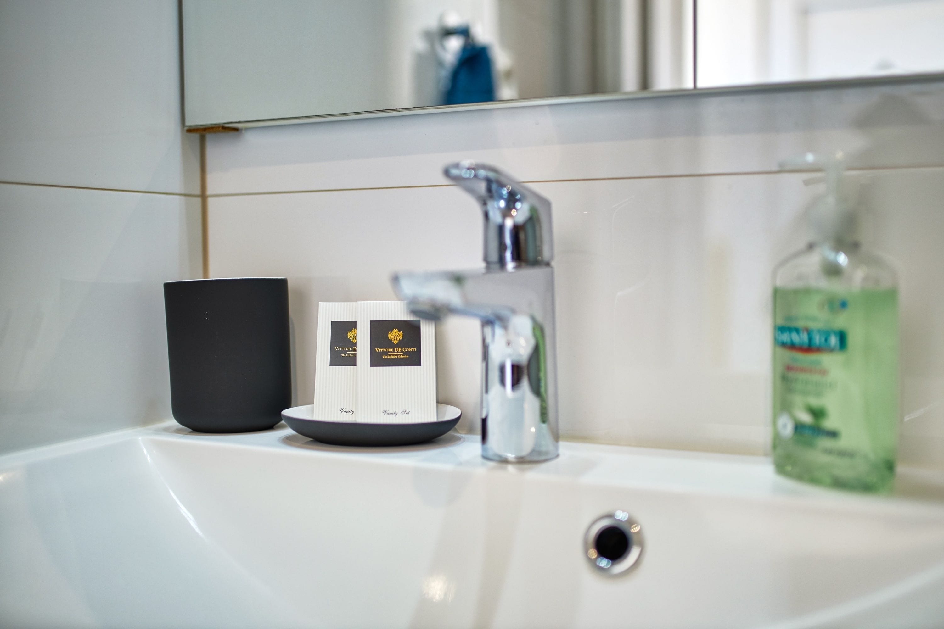 A bathroom sink with a mirror above it, a soap dispenser, and two small boxes on the sink.