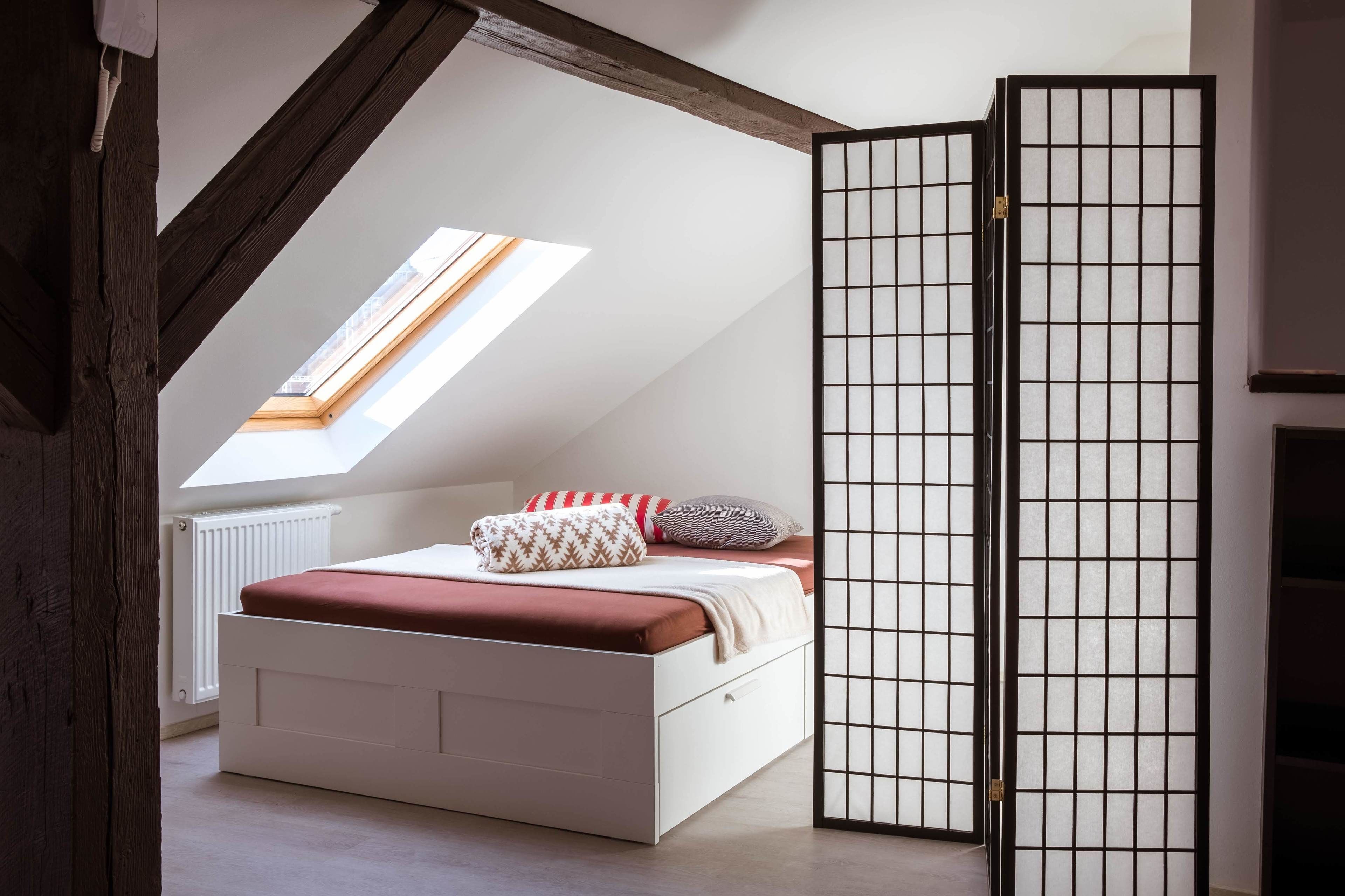 A bedroom with a sloped ceiling, a bed with a red mattress, and a view of the sky through a skylight.