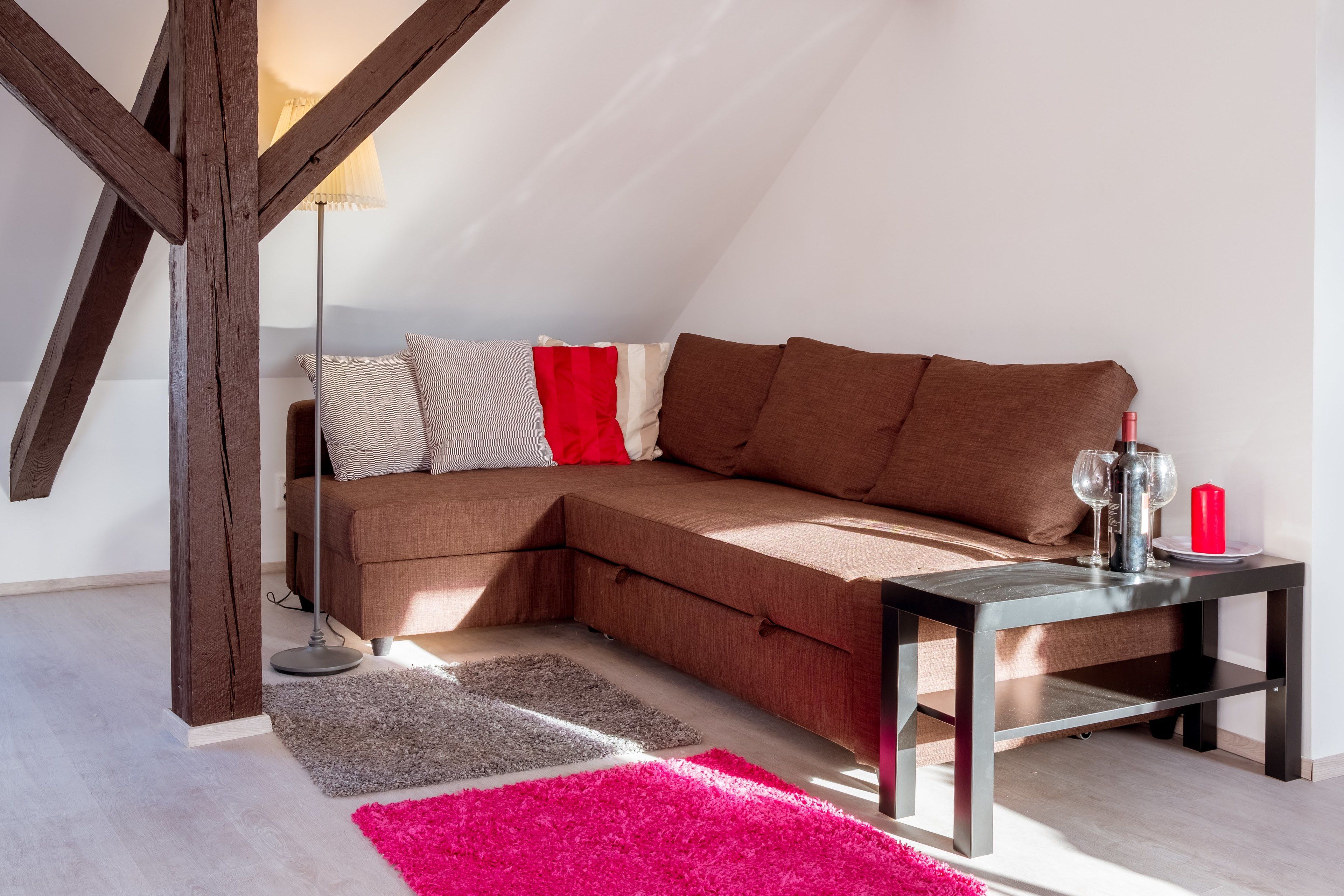 A cozy living room with a sectional sofa, a small table with a candle and glasses, and a lamp.