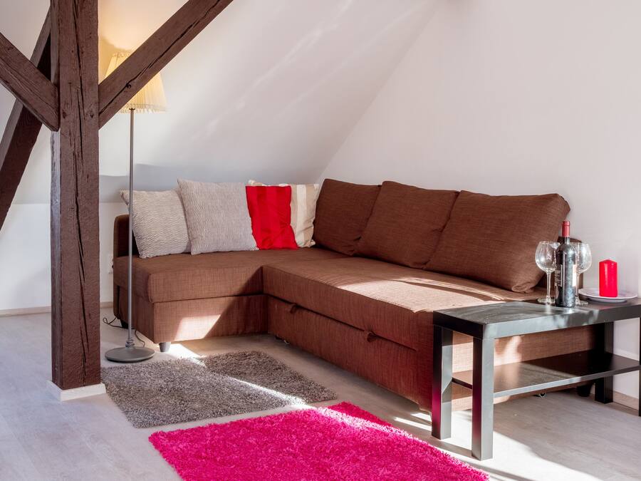 A cozy living room with a sectional sofa, a small table with a candle and glasses, and a lamp.