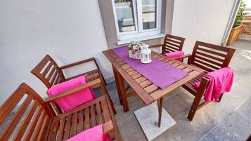 A wooden table and chairs set on a patio with a purple tablecloth, a white lantern, and a small vase with flowers.