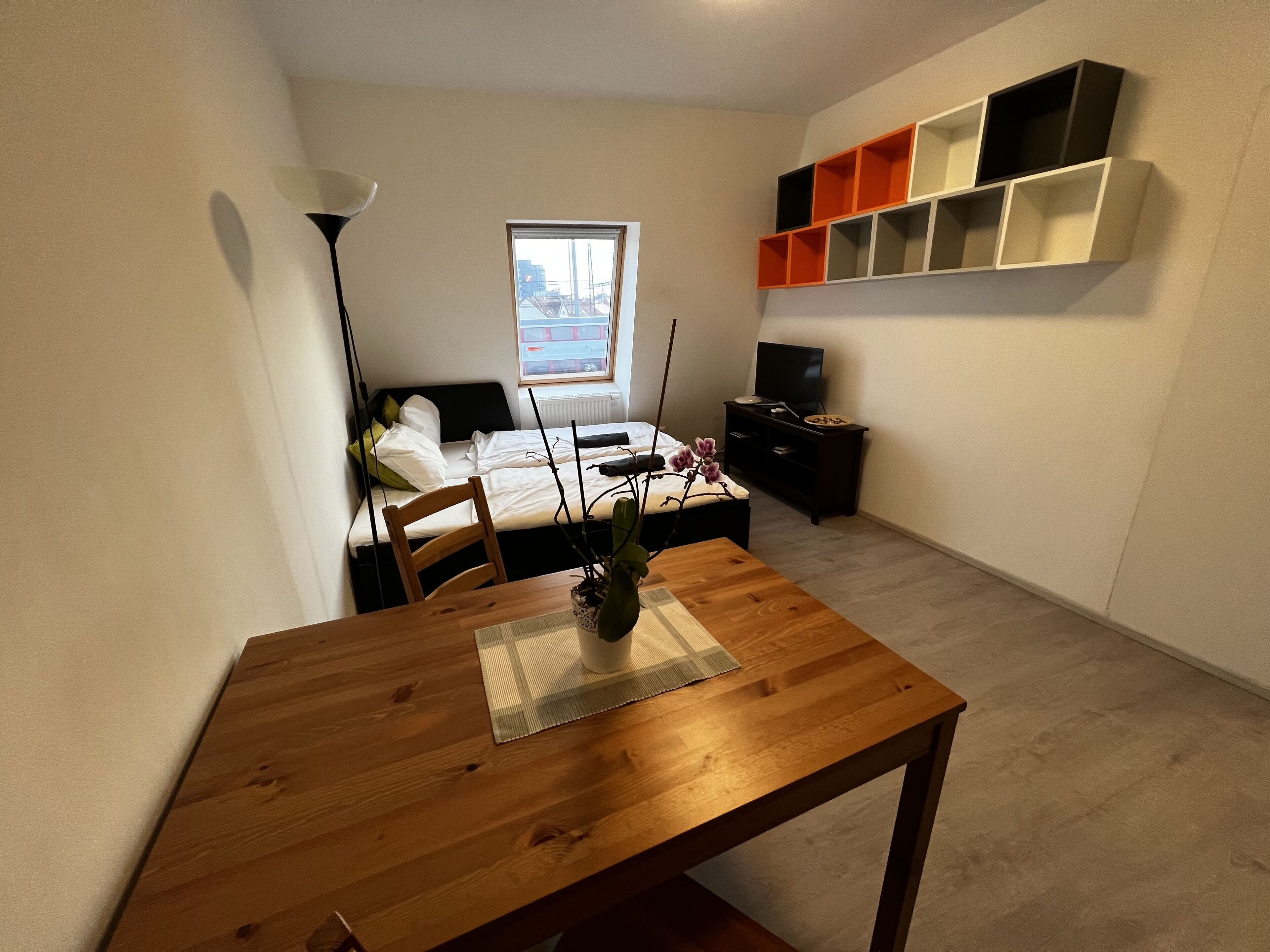 Ein kleines Schlafzimmer mit Bett, Nachttisch, Fernseher und einem Fenster mit Blick auf eine Brücke.