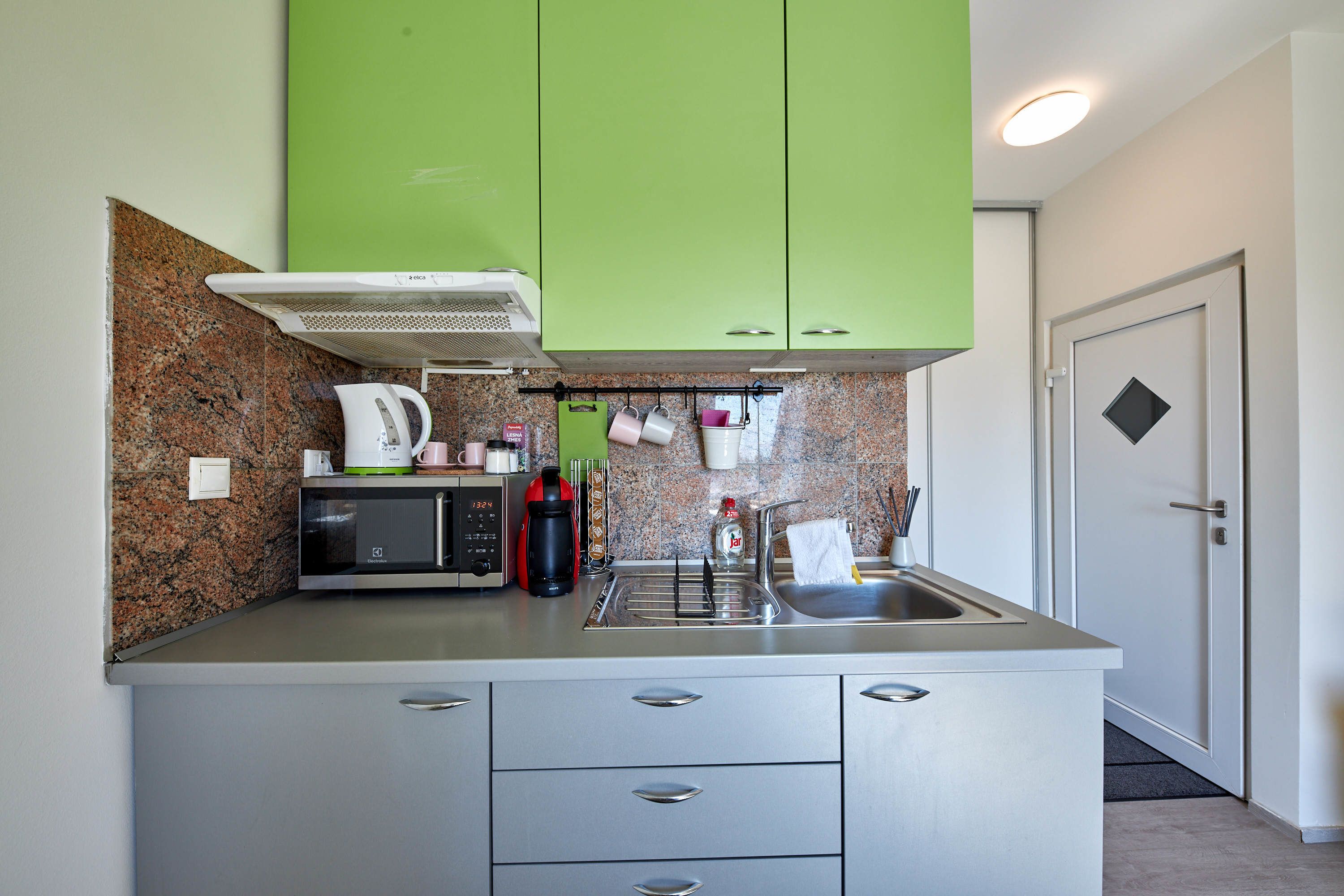 Una cocina compacta con gabinetes verdes, un microondas, una cafetera y un lavamanos.