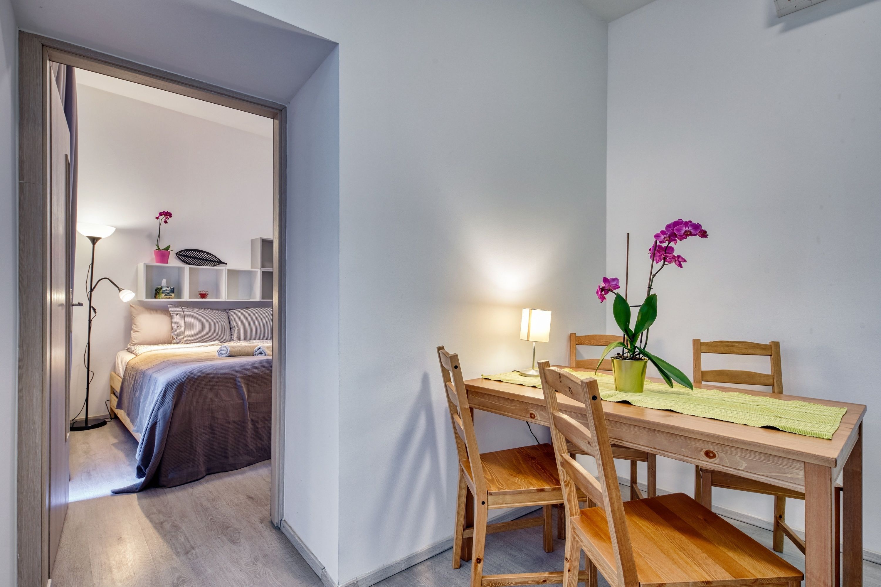 Un dormitorio con cama, mesita de noche, lámpara y una pequeña planta en maceta.