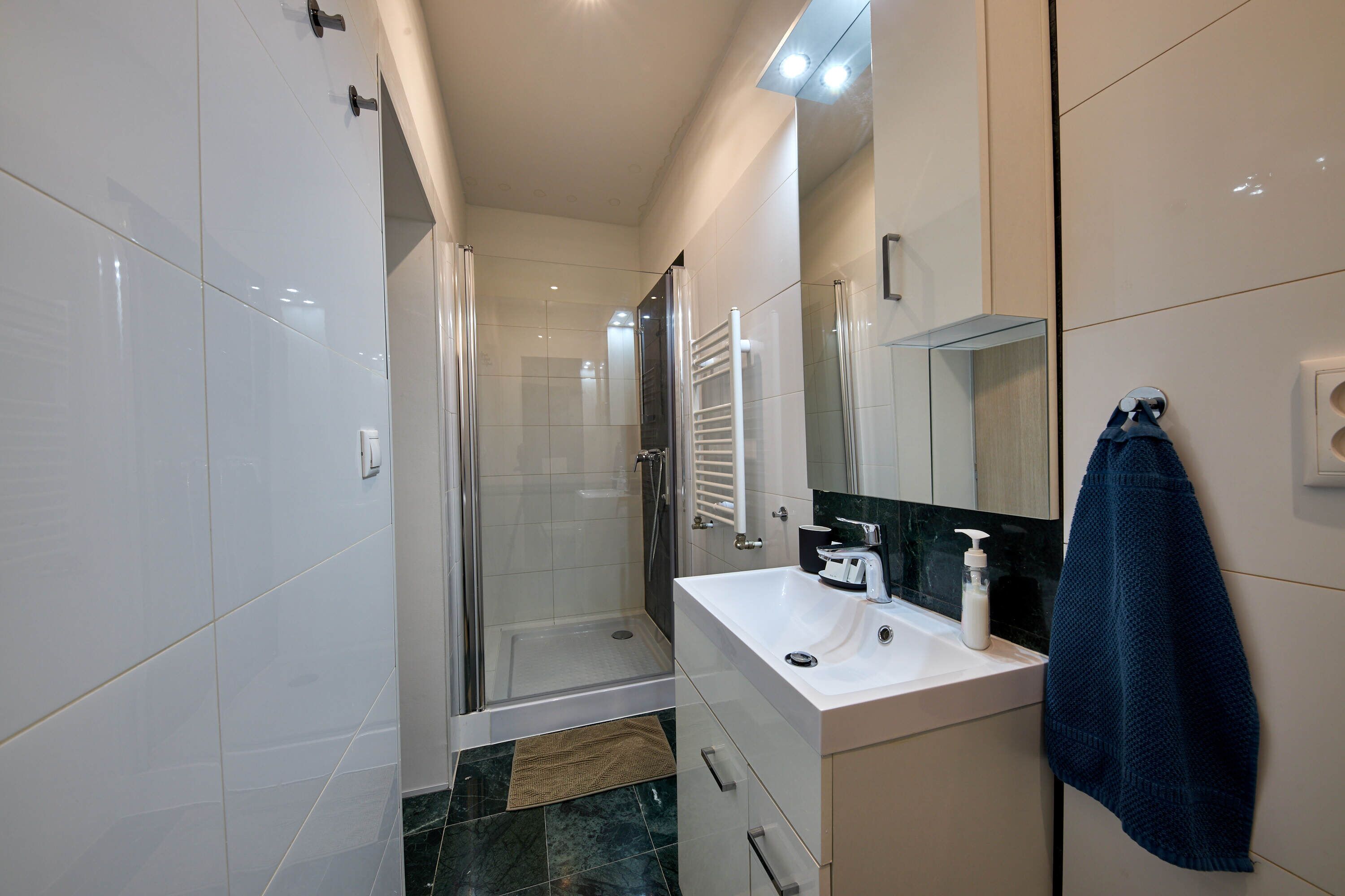 A modern bathroom with a glass shower enclosure, a white sink with a soap dispenser, and a towel hanging on the wall.