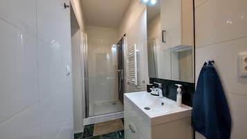 A modern bathroom with a glass shower enclosure, a white sink with a soap dispenser, and a towel hanging on the wall.