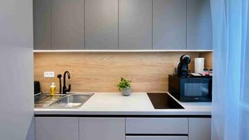 A modern kitchen with a stainless steel sink, a black coffee machine, and a microwave on the countertop.