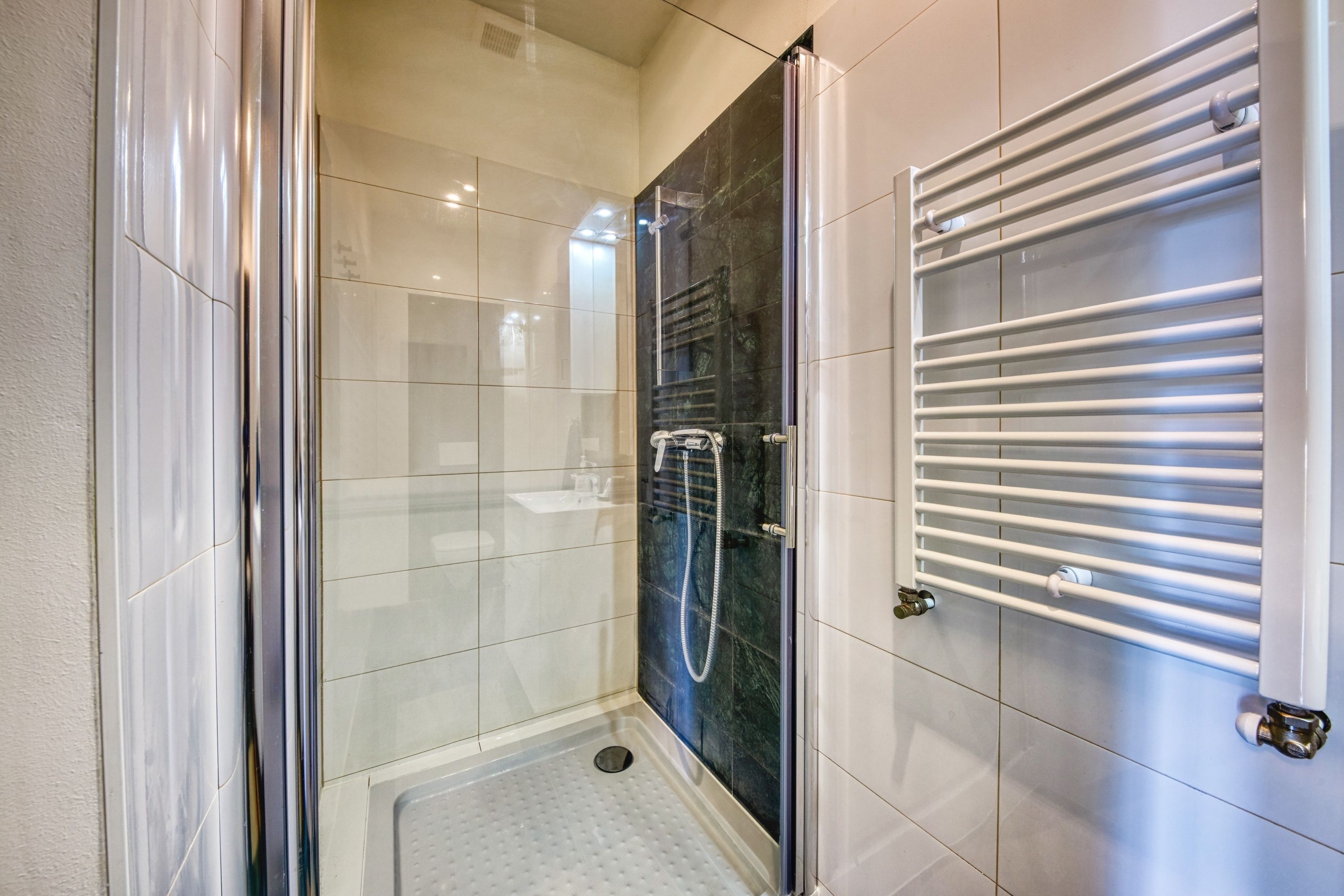 Un baño moderno con ducha acristalada, piso de baldosas blancas y toallero empotrado.