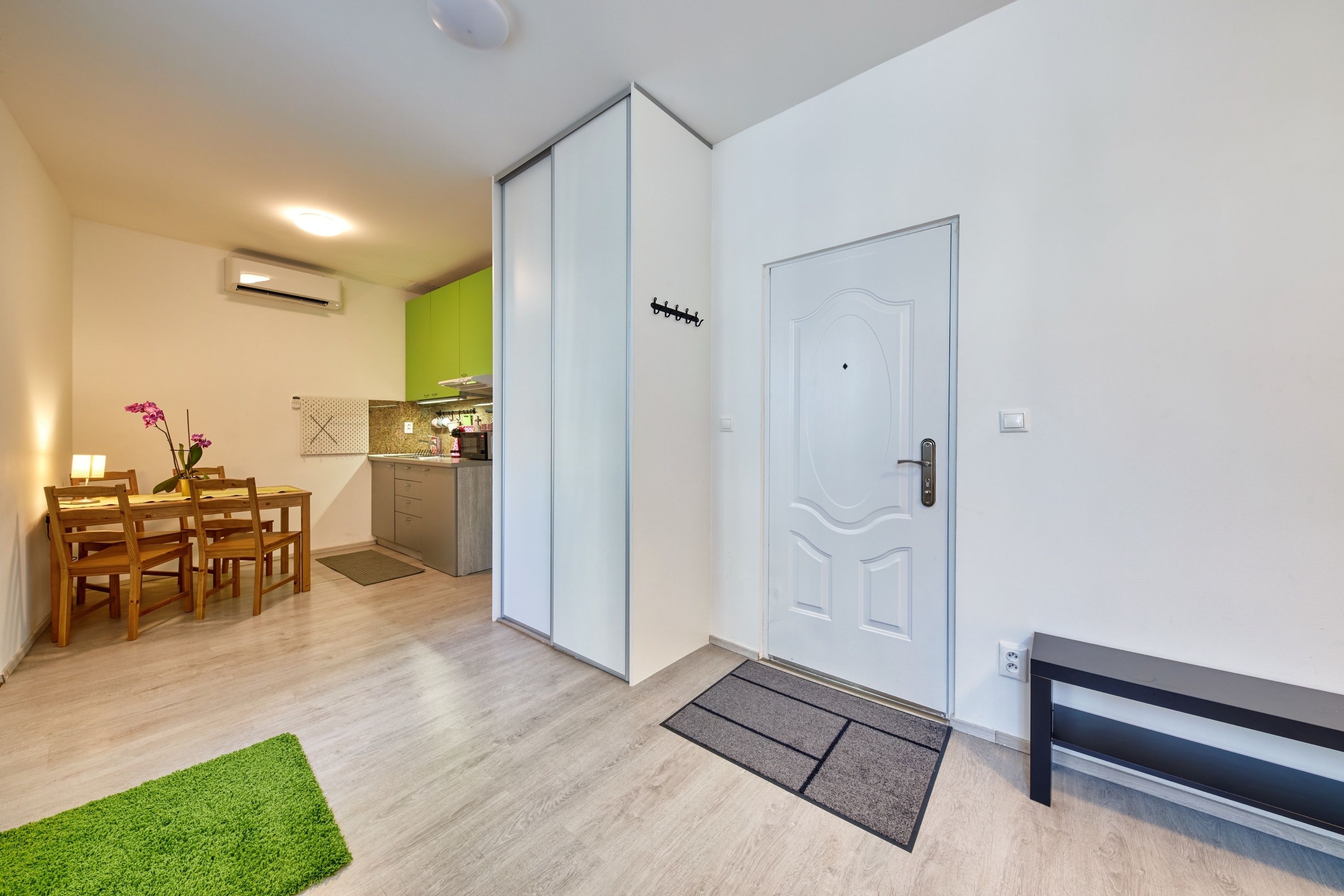 A modern apartment with a dining area, kitchen, and a door with a coat rack.