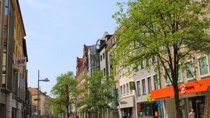 Een straat met meerlaags gebouwen, waaronder een H&M winkel en een winkel met een rood en wit bord.