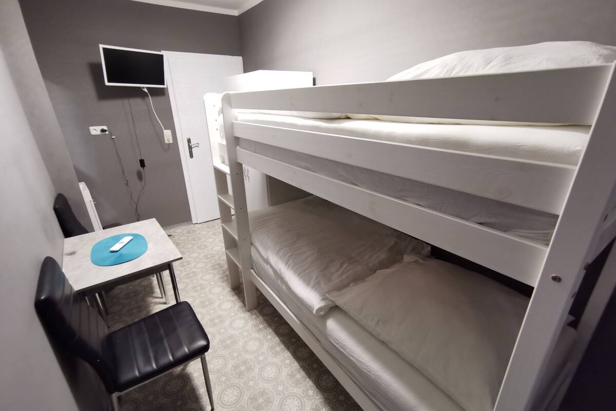A bunk bed room with a desk and chair, a television on the wall, and a door.