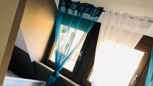Een kamer met een patroon vloer, een witte radiator, een wit wiegje en teal gordijnen bovenin vastgebonden.