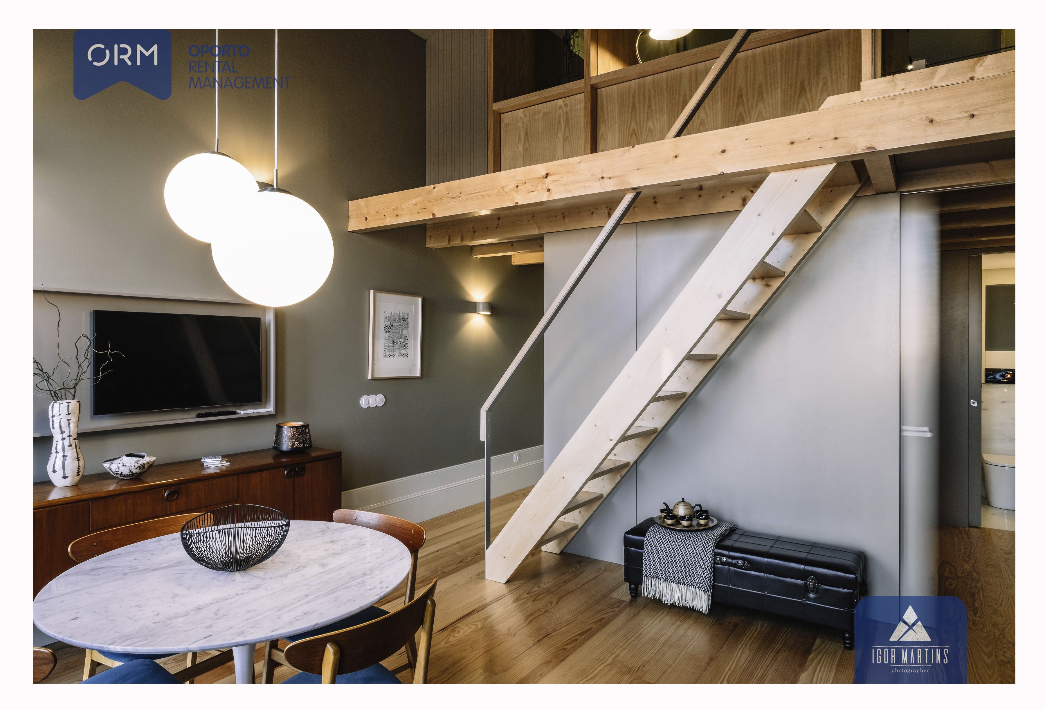 Ein modernes Interieur mit einer Holztreppe, einem runden Marmortisch und einem an der Wand befestigten Fernseher.