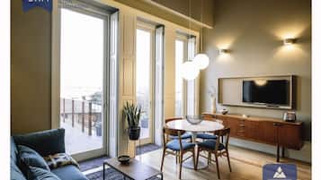Ein modernes Wohnzimmer mit einer Couch, einem Esstisch mit Stühlen, einem Fernseher und einem Balkon mit Geländer.