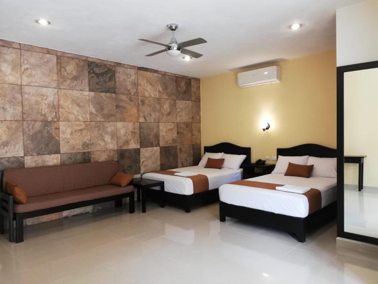 A hotel room with two beds, a sofa, a ceiling fan, and an air conditioning unit.