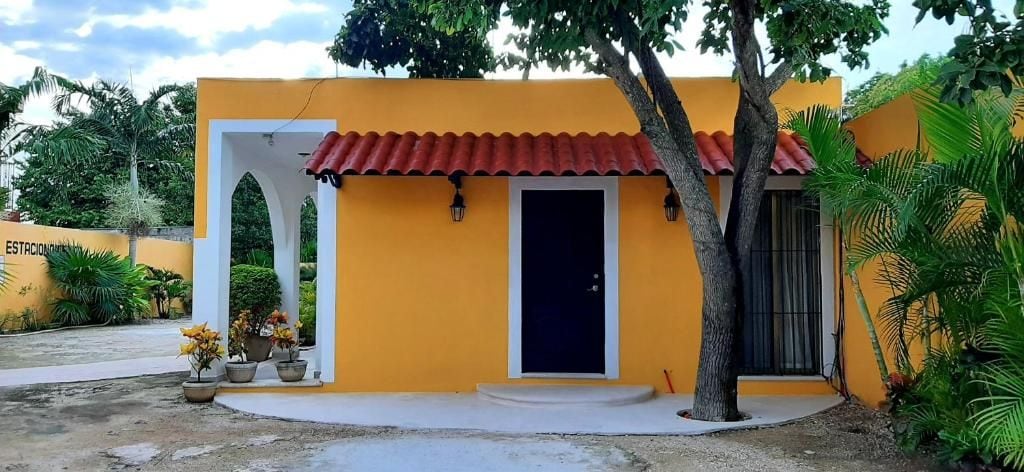 Un edificio amarillo con techo de tejas rojas, una puerta blanca y un pequeño porche.