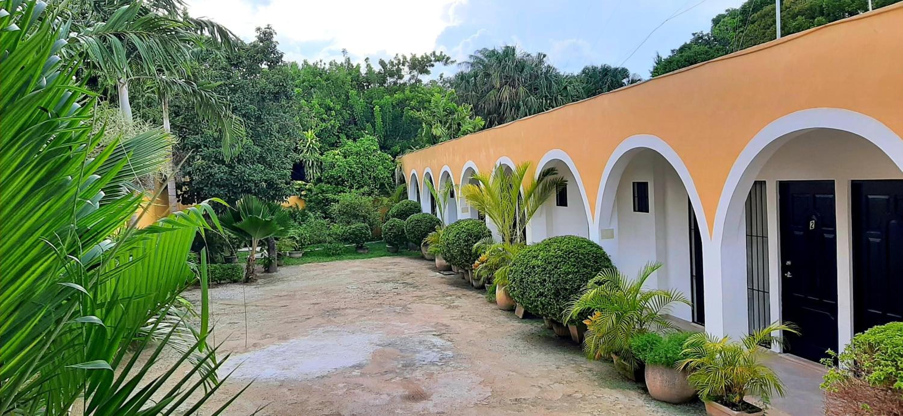 A building with a series of arched doorways, surrounded by lush greenery and potted plants.