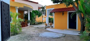 A courtyard with a yellow building, a black gate, and potted plants. - Departamentos X Kanlol (Izamal)